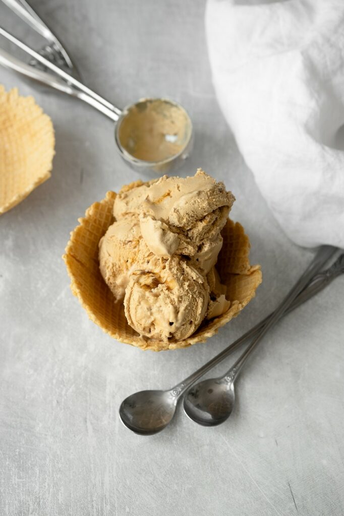 Glace vegan à la chicorée servie en boules dans une coupelle en gaufrette, vue de dessus, avec une cuillère à glace, deux petites cuillères argentées et un torchon blanc.