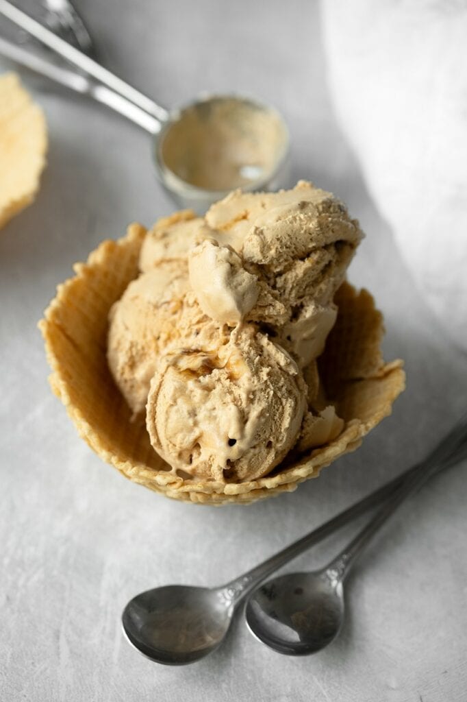Boules de glace vegan à la chicorée aux reflets caramel dans une coupelle en gaufrette croustillante, avec deux petites cuillères argentées posées devant.