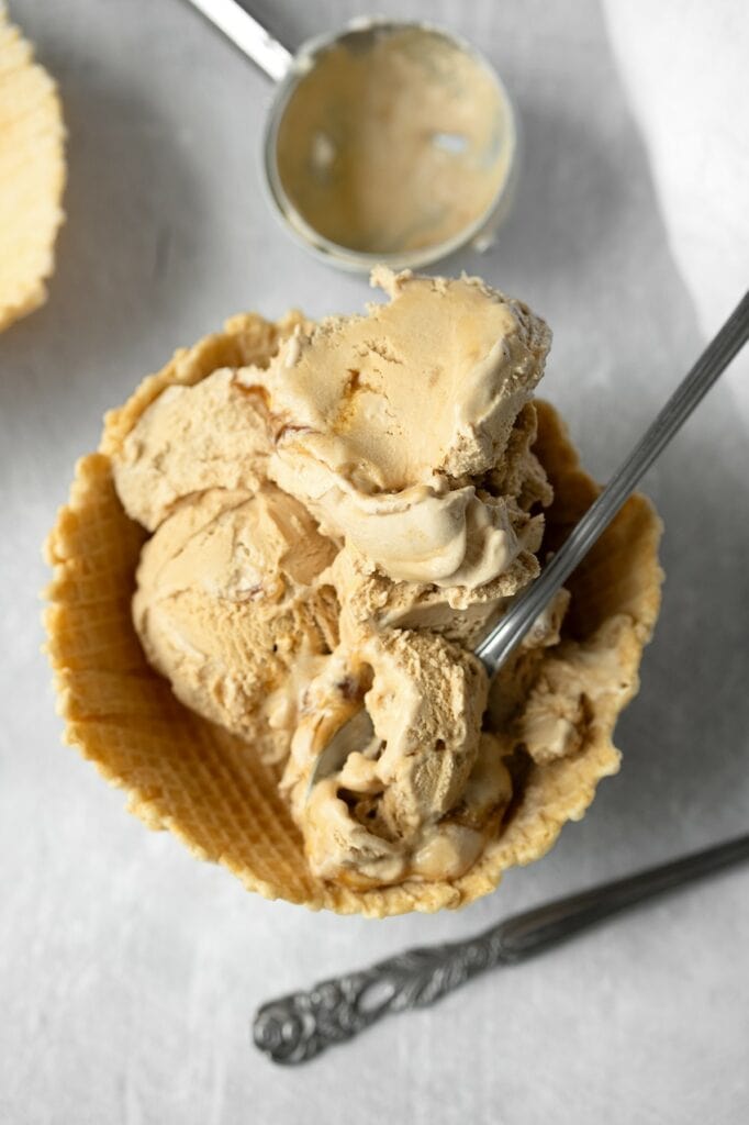 Vue de dessus d'une glace vegan à la chicorée dans une coupelle en gaufrette, avec une cuillère plantée dans la glace révélant sa texture crémeuse et ses marbrures caramel.