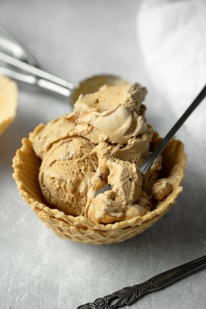 Gros plan sur la texture onctueuse d'une glace vegan à la chicorée dans une coupelle en gaufrette, avec une cuillère plongée dans la glace couleur caramel.